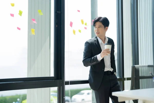 Azjatycki Biznesmen Pijący Kawę Wyglądający Przez Okno Biurze Atrakcyjny Biznesmen — Zdjęcie stockowe