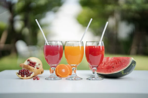 Orange juice, pomegranate juice and watermelon juice on the natural background in the garden.