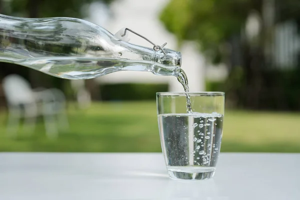 Pour the water from the water bottle into the glass in the garden around the house.