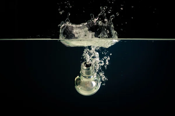 En glödlampa som faller i klart vatten med mörk bakgrund Stockfoto