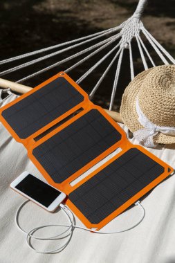 Akıllı telefon yaz kampında güneş pilinden şarj oluyor. Kampta kullanmak için zayıf enerji. Gadget 'lar ve güneş şapkaları bir hamakta yatıyor..