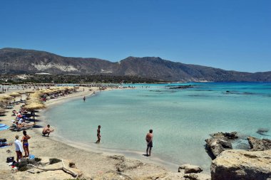 Elafonisi plajı, Girit - 18 Haziran 2021: Muhteşem turkuaz suyu ve kırmızı / pembe kumla tropikal plajı görmek