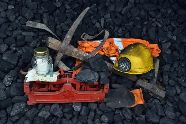 The miner belongings (helmet, gloves, pickaxe, vest, belt), graveyard candle and coal on the weight as concept after the fatal accident in the mine