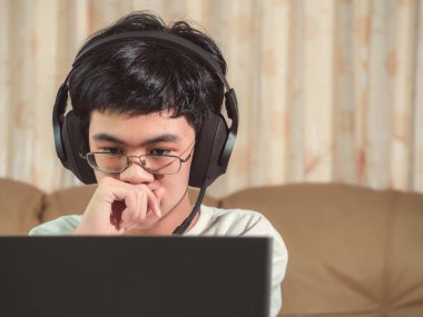 İnternetten ders öğrenirken kulaklık takan liseli çocuk çalışmak için dizüstü bilgisayara bakıyor. Uzaklık ve eğitim öğrenimi evde kalır.