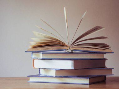 Pek çok kitabın basit bir kompozisyonu, ahşap masa üzerindeki kitap yığını veya yığını, bir tanesi kopya alanı ile açılır.