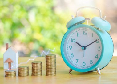Hand are stacking coins with alarm clock to save the financial stability for the future. Concept for loan, property ladder, financial, mortgage, real estate investment, taxes and bonus.
