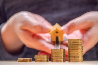 Ev veya ev modeli ve sikkeler üzerinde el ile ev anahtarı. Kavramı kredi için mülkiyet merdiven, finans, mortgage, gayrimenkul yatırım, vergiler ve bonus.