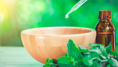 Nane şekeri özü, küçük bir şişede, ahşap masanın üzerinde nane yaprağı yanında. Cam damlacıktan organik biyo-alternatif tıbba dökülen temel yağ, kahverengi şişe..