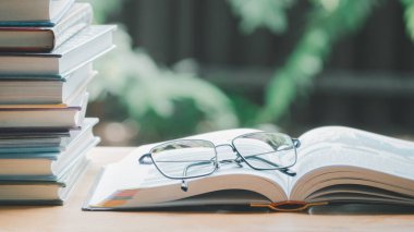 Ahşap masa üzerinde bir sürü kitap, yığın ya da yığın basit bir kompozisyon, bunlardan biri açık ve ikonlu gözlük yenilenebilir konsept için CO2 ve enerji kaynakları tasarrufu.