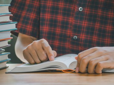 Asyalı genç bir adam, kitap yığınlarının yanındaki bir kitabı açıyor, okuyor ve parka özenle bakıyor..