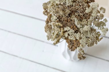 Beyaz, kahverengi, bej renginde çiçeklerle dolu bir vazo, ahşap bir arka planda.