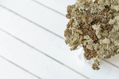 Beyaz ahşap arka planda beyaz bir vazoda beyaz, kahverengi ve bej renkli çiçeklerden oluşan bir buket. Kart, İç dekorasyon.