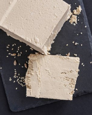 Büyük bir parça susam halkası siyah servis tahtasının üzerinde duruyor, bir parça tamamen kesilmiş.