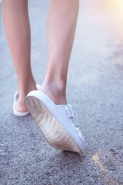 Beyaz parmak arası terlikli kadın bacakları. Asfaltta gün ışığıyla güzel ince bacaklar. Ayaklar dışarı.