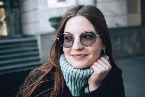 Hermosa mujer con pecas y pelo largo en un abrigo oscuro sentado en un café en la calle —  Fotos de Stock