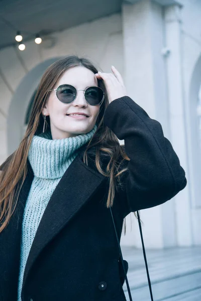 Mujer sonriente con el pelo largo en un abrigo oscuro camina por la calle —  Fotos de Stock