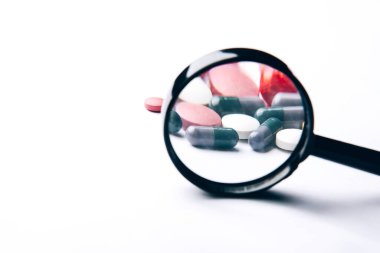Dietary supplements and pills for dieting. Vitamin tablets and a magnifying glass on a white background. Medical concept. Complementary and medical products