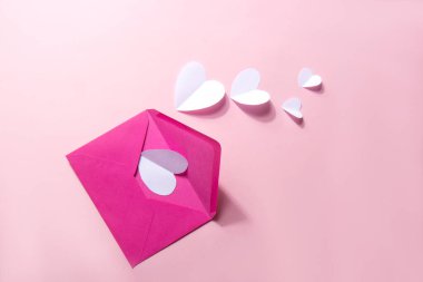 Üzerinde pembe arka planda beyaz kağıt kalpler olan pembe bir zarf. Sevgililer Günü geçmişi. Beyaz hacimli kağıt kalpler. Sevgililer Günü konsepti