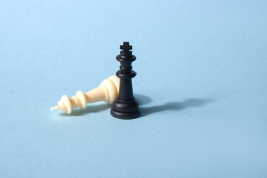 Mavi arka planda iki siyah-beyaz satranç taşı ve bir tanesi düşmüş. Soyut arkaplan. Satranç taşı. Liderlik kavramı