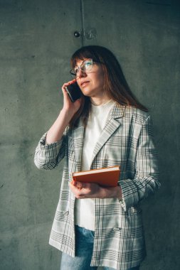 Ofisinde cep telefonu ve turuncu not defteri olan gözlüklü genç bir iş kadını.