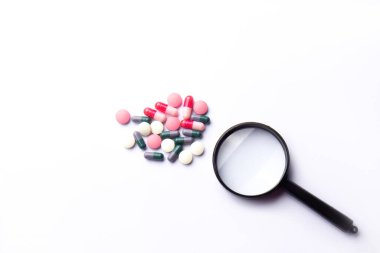 Vitamin hapları ve beyaz arka planda büyüteç. Beslenme takviyeleri ve diyet için haplar. Tıbbi konsept. Tamamlayıcı ve tıbbi ürünler