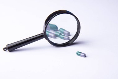 Vitamin hapları ve beyaz arka planda büyüteç. Beslenme takviyeleri ve diyet için haplar