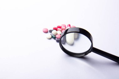 Çok renkli kapsüller, pil ve beyaz arka planda bir büyüteç. Beslenme takviyeleri ve diyet için haplar. Tıbbi konsept. Tamamlayıcı ve tıbbi ürünler. Seçici odak