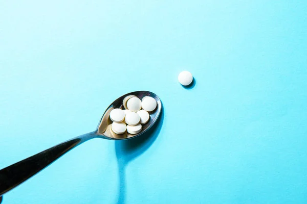 Dietary supplements. White vitamin tablets on iron spoon on a blue background