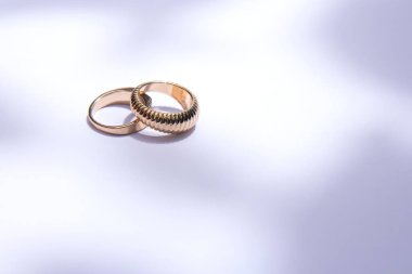 Yaprakların zıt gölgeleriyle beyaz arka planda iki altın alyans.