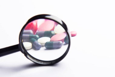 Çok renkli kapsüller, pil ve beyaz arka planda bir büyüteç. Beslenme takviyeleri ve diyet için haplar. Tıbbi konsept. Tamamlayıcı ve tıbbi ürünler. Seçici odak