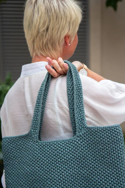 Woman holds a handmade knitted bag in her hand outdoors. Sustainable shopping. Wasteless lifestyle. Female with a jute bag with her own hands on a walk