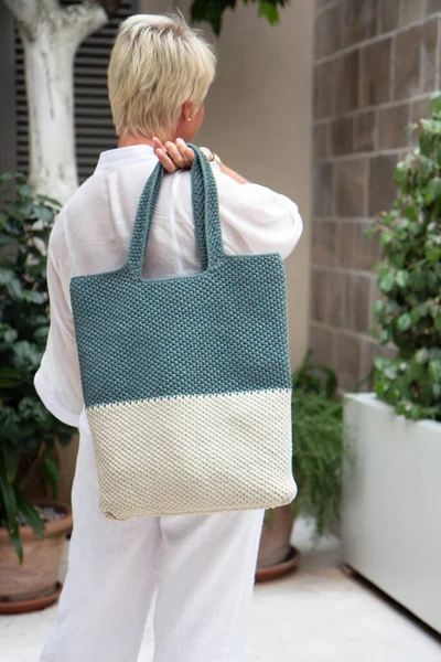 Woman holds a handmade knitted bag in her hand outdoors. Sustainable shopping. Wasteless lifestyle. Female with a jute bag with her own hands on a walk