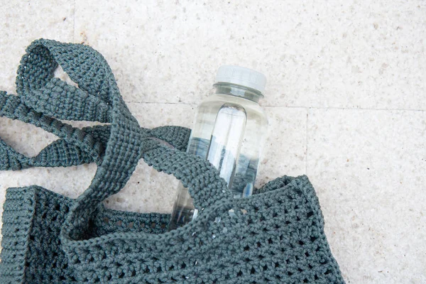 Blue knitted bag handmade and a bottle of water outdoors. Sustainable shopping. Waste-fr ee lifestyle. Do-it-yourself jute bag