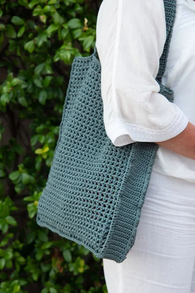 Woman holds a handmade knitted bag in her hand outdoors. Sustainable shopping. Wasteless lifestyle. Female with a jute bag with her own hands on a walk