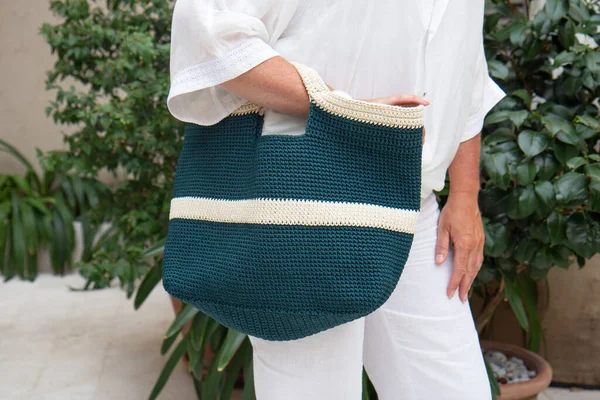 Woman holds a handmade blue knitted bag in her hand outdoors. Sustainable shopping. Wasteless lifestyle. Female with a jute bag with her own hands on a walk