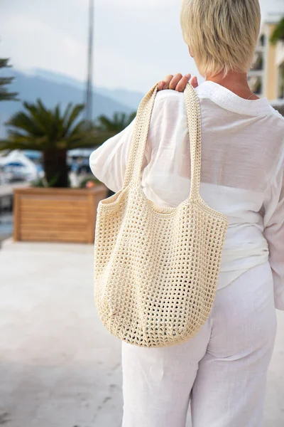 Woman holds a handmade beige knitted bag in her hand outdoors. Sustainable shopping. Wasteless lifestyle. Female with a jute bag with her own hands on a walk