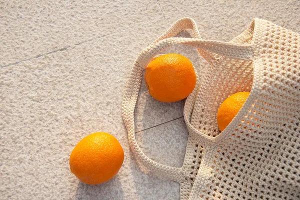 Beige knitted bag handmade and ripe oranges outdoors. Sustainable shopping. Waste-fr ee lifestyle. Do-it-yourself jute bag