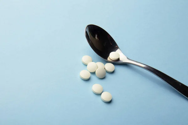 White vitamin tablets on iron lack spoon on a blue background. Dietary supplements. Complementary and medical products