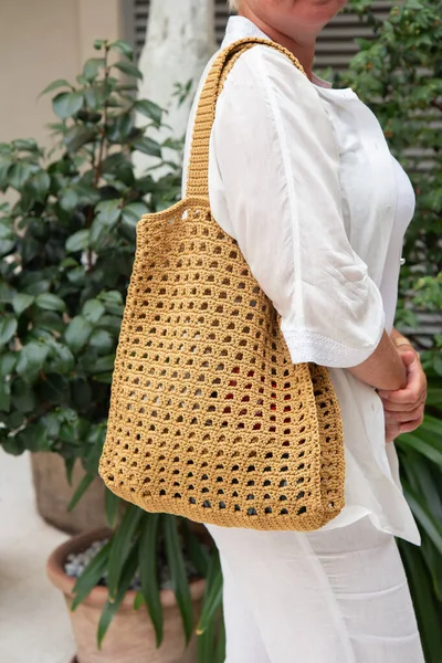 Woman holds a handmade beige knitted bag in her hand outdoors. Sustainable shopping. Wasteless lifestyle. Female with a jute bag with her own hands on a walk. Close up