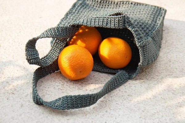 Grey knitted bag handmade and ripe oranges outdoors. Sustainable shopping. Waste-fr ee lifestyle. Do-it-yourself jute bag