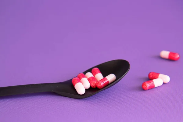 Vitamin tablets on black spoon on a violet background. Dietary supplements. Complementary and medical products