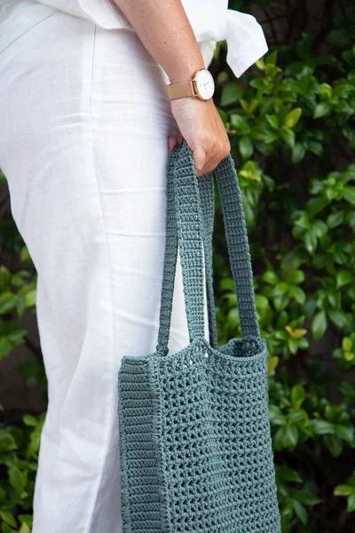 Woman holds a handmade blue knitted bag in her hand outdoors. Sustainable shopping. Wasteless lifestyle. Female with a jute bag with her own hands on a walk. Close up