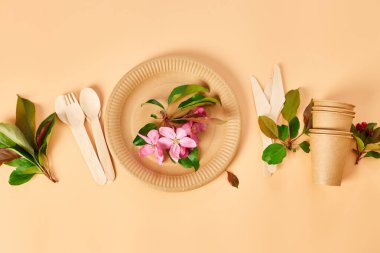Çiçekli, sıfır atık, plastiksiz, çevre dostu, kağıt bardaklar, tabaklar, pastel turuncu arka planda ahşap çatal bıçak takımı. Geri dönüşüm ve plastik içermeyen konsept.