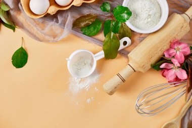 Çiçekli fırın ya da yemek çerçevesi, malzemeler, pastel turuncu arka planda hamur işi için mutfak malzemeleri, bahar pişirme teması. Üst görünüm, alanı kopyala.