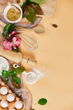 Bakery  or cooking frame with flower, ingredients, kitchen items for pastry on pastel orange background,  spring cooking theme. Top view, copy space.