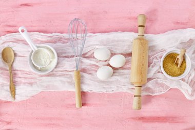 Çiçekli fırın veya yemek iskeleti, malzemeler, pembe arka planda hamur işi için mutfak malzemeleri, bahar pişirme teması. Üst görünüm, alanı kopyala.