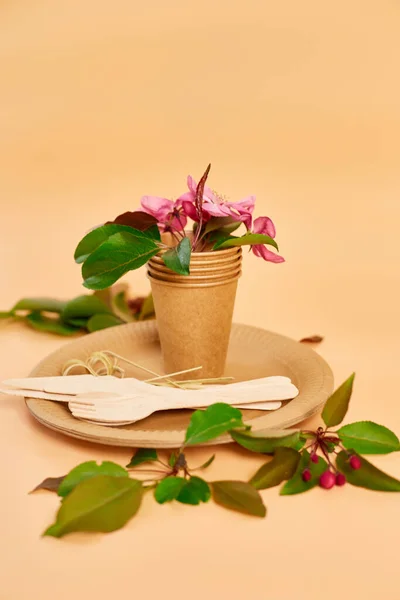 Flat lay of eco craft paper tableware with flowers, Zero waste, plastic free, eco friendly, paper cups, dishes, plates and wooden cutlery on pastel orange background. Recycling and plastic free concept.