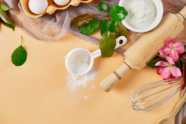 Çiçekli fırın ya da yemek çerçevesi, malzemeler, pastel turuncu arka planda hamur işi için mutfak malzemeleri, bahar pişirme teması. Üst görünüm, alanı kopyala.