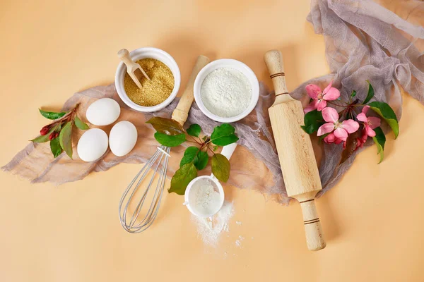 Çiçekli fırın ya da yemek çerçevesi, malzemeler, pastel turuncu arka planda hamur işi için mutfak malzemeleri, bahar pişirme teması. Üst görünüm, alanı kopyala.