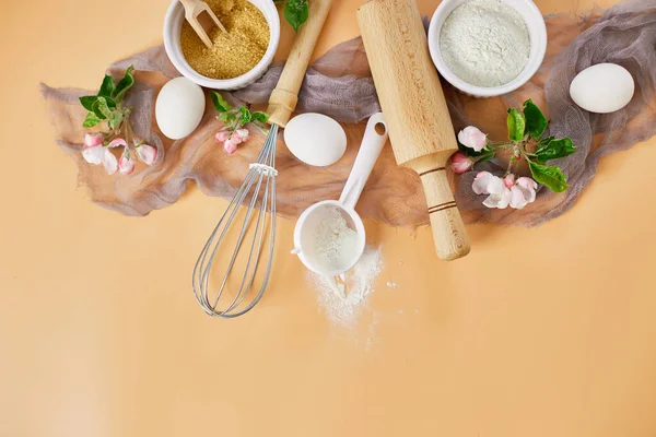 Çiçekli fırın ya da yemek çerçevesi, malzemeler, pastel turuncu arka planda hamur işi için mutfak malzemeleri, bahar pişirme teması. Üst görünüm, alanı kopyala.